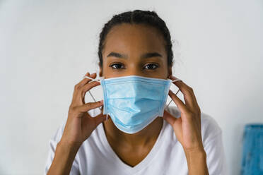 Young girl wearing protective face mask standing against wall - MGIF01036