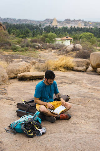 Junger Mann liest ein Buch, während er auf dem Boden sitzt, Karnataka, Hampi, Indien, lizenzfreies Stockfoto