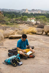 Junger Mann liest ein Buch, während er auf dem Boden sitzt, Karnataka, Hampi, Indien - JMPF00463