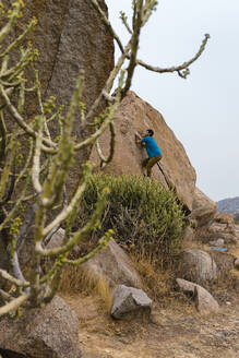 Adventurous young man climbing rocky mountain, Karnataka, Hampi, India - JMPF00464