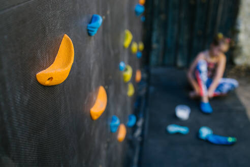 Unrecognizable blurred girl sitting near climbing wall with plastic grips in contemporary gym - ADSF16781