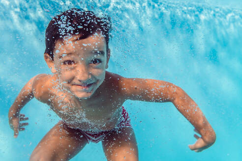 Unterwasseransicht eines begeisterten Kindes, das im klaren Wasser des Pools schwimmt und in die Kamera schaut - ADSF16817