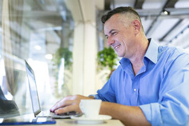 Smiling businessman using laptop while sitting at cafe - WPEF03434