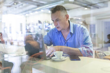 Männlicher Unternehmer, der einen Laptop benutzt, während er mit einem Kaffee im Café sitzt - WPEF03448