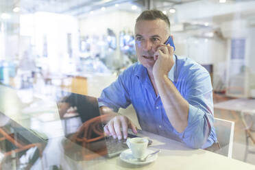 Male professional talking on mobile phone while sitting with laptop and coffee in cafe - WPEF03450