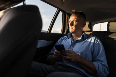 Mature male professional looking away while sitting with smart phone in car - WPEF03463