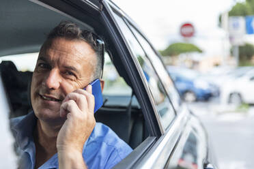 Lächelnder männlicher Berufstätiger, der im Auto sitzend über sein Handy spricht - WPEF03466