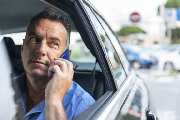 Älterer männlicher Unternehmer, der im Auto sitzend über sein Handy spricht - WPEF03467