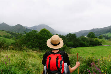 Rückenansicht eines nicht erkennbaren Touristen mit Rucksack und Hut, der auf einem Waldweg steht und wegschaut - ADSF16826