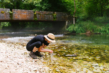 Side view of female tourist drinking clear water from calm river in forest during summer adventure - ADSF16829