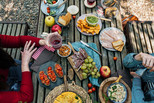 Hoher Winkel von nicht erkennbaren Freundinnen, die an einem Holztisch im Wald sitzen und bei einem Picknick im Valle del Jerte im Sommer leckeres Essen essen - ADSF16837