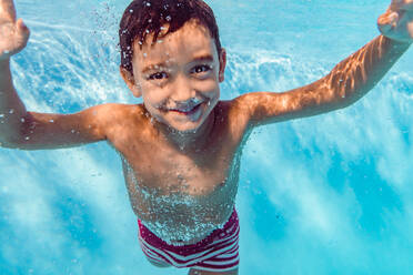 Unterwasseransicht eines begeisterten Kindes, das im klaren Wasser des Pools schwimmt und in die Kamera schaut - ADSF16845