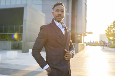 Seriöser afroamerikanischer männlicher Unternehmer im eleganten Anzug, der mit der Hand in der Tasche auf der Straße im Stadtzentrum steht und wegschaut - ADSF16892