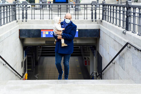 Man with face mask carrying baby while walking on staircase in city - PGF00147