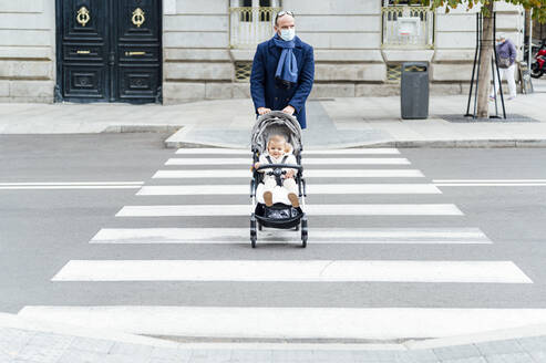 Mann mit Gesichtsmaske geht mit Kinderwagen über die Straße in der Stadt - PGF00152