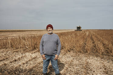 Smiling farmer standing with hands in pockets at soybean farm - ZEDF03980