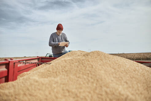 Landwirt mit digitalem Tablet, während er auf einem Traktor gegen den klaren Himmel steht - ZEDF03992