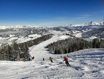 Österreich, Salzburg, St. Johann im Pongau, Skifahrer fahren in den schneebedeckten Bergen den Hang hinunter - WWF05457