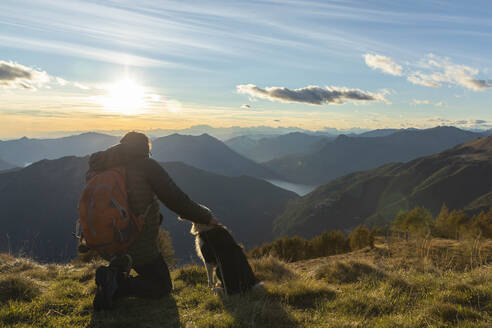 Wanderer kniend beim Streicheln des Hundes auf dem Berggipfel bei Sonnenuntergang - MCVF00630