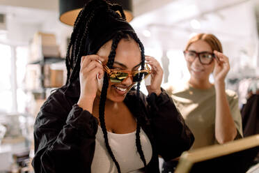 Smiling female friends trying eyewear while talking at fashion store - MASF19962