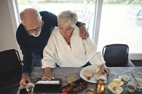 High angle view of senior couple looking at digital tablet while sitting by dining table in living room - MASF19973