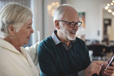 Smiling senior couple using smart phone while sitting in living room - MASF19981