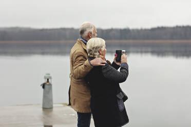 Älteres Paar, das sich am See vor einem klaren Himmel fotografieren lässt - MASF19984