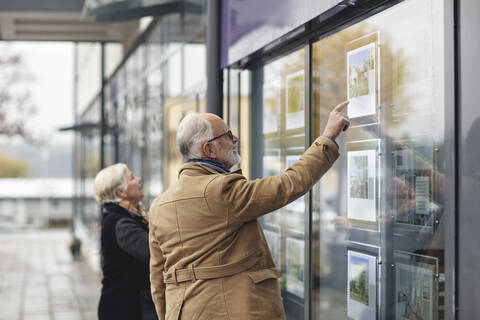 Älterer Mann, der von seiner Partnerin im Winter in der Stadt auf ein Glasfenster zeigt, lizenzfreies Stockfoto