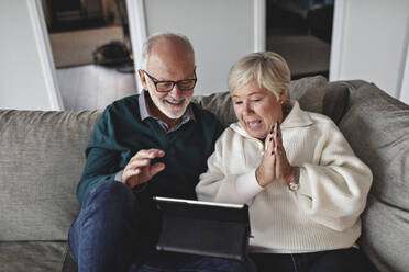 Lächelndes älteres Ehepaar, das ein digitales Tablet benutzt, während es auf dem Sofa im Wohnzimmer sitzt - MASF19995