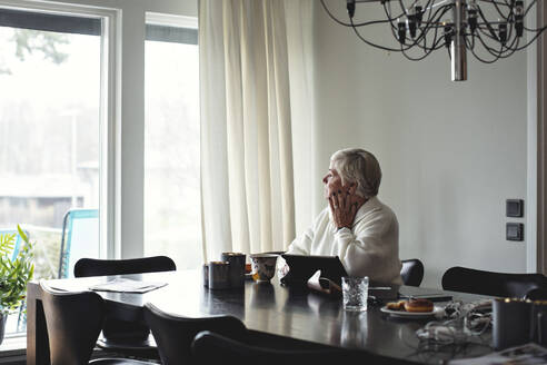 Senior woman looking away while sitting by dining table at home - MASF20009