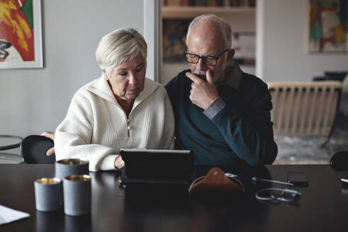 Älteres Ehepaar benutzt ein digitales Tablet, während es am Esstisch im Wohnzimmer sitzt - MASF20013