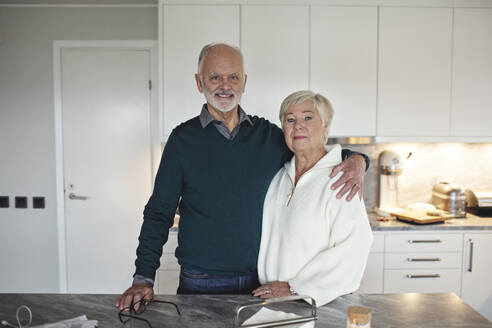 Portrait of senior couple standing by kitchen island at home - MASF20014