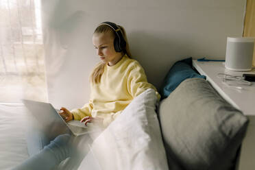Mädchen mit Kopfhörern und Laptop auf dem Bett sitzend - MASF20020