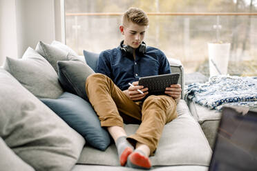 Teenage boy using digital tablet while sitting on sofa at home - MASF20030