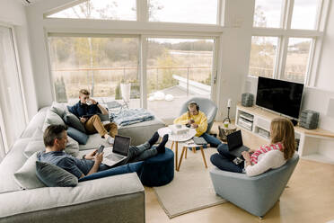 Blick von oben auf die Familie, die im Wohnzimmer sitzend Technik benutzt - MASF20032