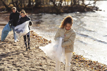 Environmentalist with male and female friends collecting plastic waste by lake - MASF20035