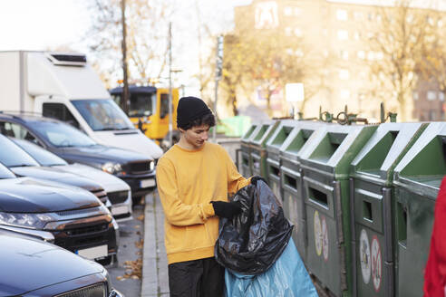 Junger männlicher Freiwilliger hält Abfall in einer Plastiktüte neben einem Mülleimer - MASF20038