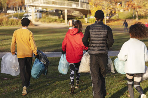 Rückansicht von jungen Umweltschützern, die mit Plastikmüll im Park spazieren gehen - MASF20042
