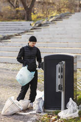 Male environmentalist with plastic waste standing by garbage can - MASF20043