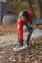 Lächelnde Umweltschützerin sammelt im Herbst Plastikmüll im Park - MASF20049