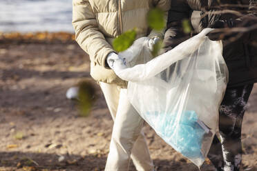 Midsection of female environmentalists holding plastic filled with garbage by lake - MASF20052