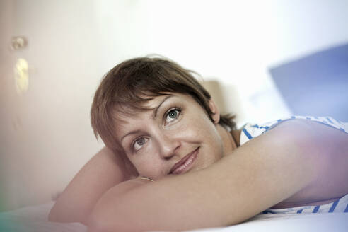 Thoughtful woman looking away while lying down in bedroom at home - AJOF00308