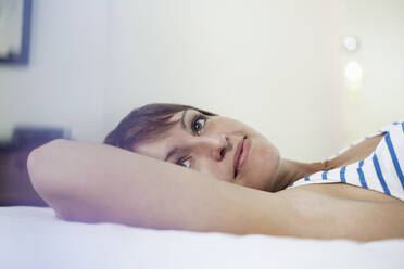 Contemplating woman looking away while lying down in bedroom at home - AJOF00309