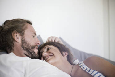 Lächelndes heterosexuelles Paar, das sich zu Hause im Schlafzimmer auf dem Bett ausruht - AJOF00314
