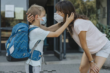 Mother and son wearing protective mask standing face to face in front of school building - MFF06363