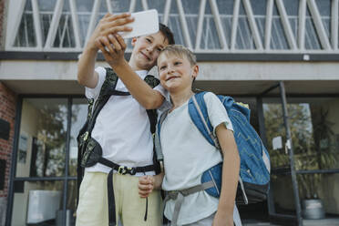 Brüder machen ein Selfie mit ihrem Smartphone, während sie vor einem Schulgebäude stehen - MFF06367