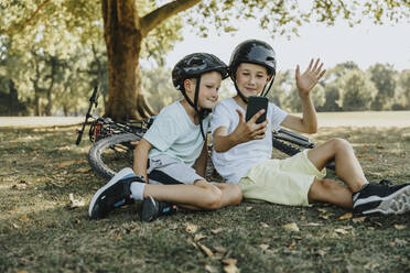 Brüder führen einen Videoanruf auf einem Smartphone in einem öffentlichen Park - MFF06374