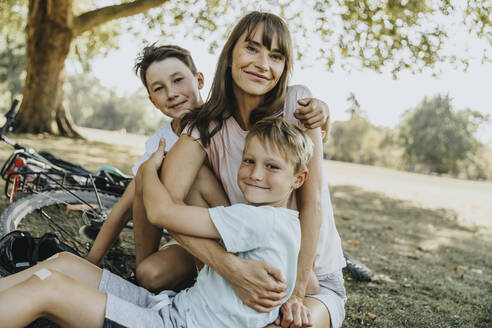 Mother embracing sons while sitting in public park - MFF06382