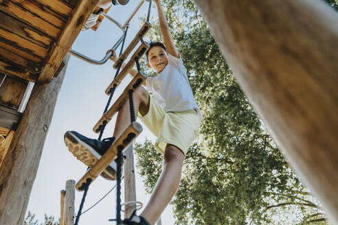 Junge klettert auf Leiter in öffentlichem Park an sonnigem Tag - MFF06386