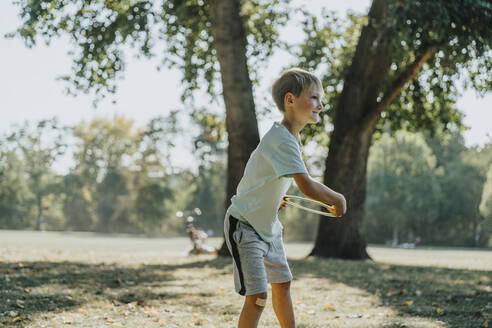 Little boy throwing frisbee ring while standing in public park on sunny day - MFF06408